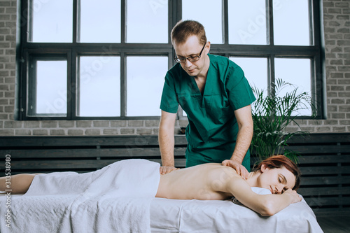 Massage therapist doing massotherapy of a young woman, elbow joint massage. Beautiful relaxed face of a young woman with brown hair and closed eyes. © Eno1