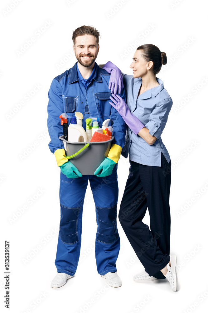 A young bearded smiling man in the uniform of a janitor holds a basket with moisturizing products, and maid-shaped women lean on his shoulder. Isolated on a white background A young bearded smiling man in the uniform of a janitor holds a basket with moisturizing products, and maid-shaped women lean on his shoulder. Isolated on a white background