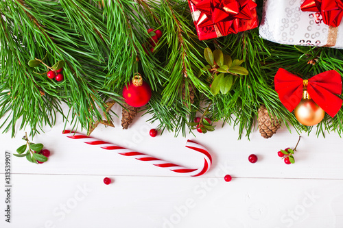 Christmas pine tree with decoration, red berries, gift box, candy cane, cones on a white wooden background. Christmas greeting card. Text space.