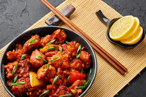 Fish Manchurian dry looks like Schezwan Fish in black bowl at dark slate background. Fish Manchurian - is indo chinese cuisine dish with deep fried salmon, bell peppers, sauce and onion. photo