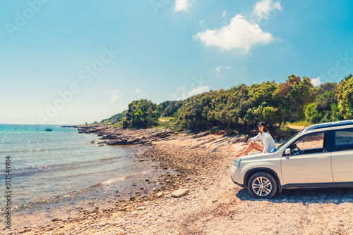 woman sitting on car hood at summer beach vacation concept