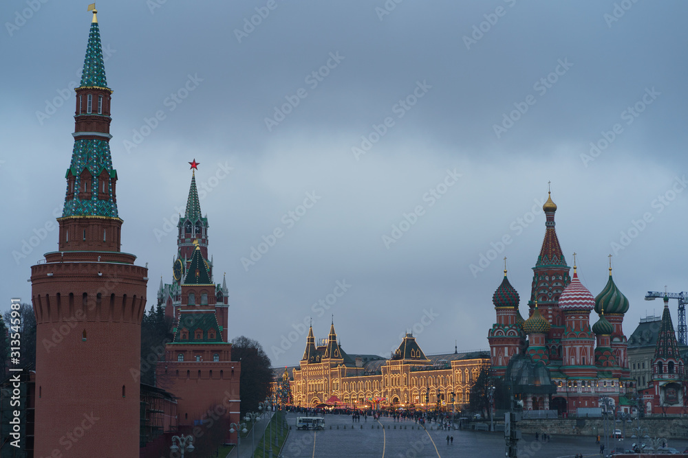 Brightly illuminated Red Square, facades of the GUM (Central Department store), Saint Basil's Cathedral, Spasskaya tower of Kremlin and walking people.