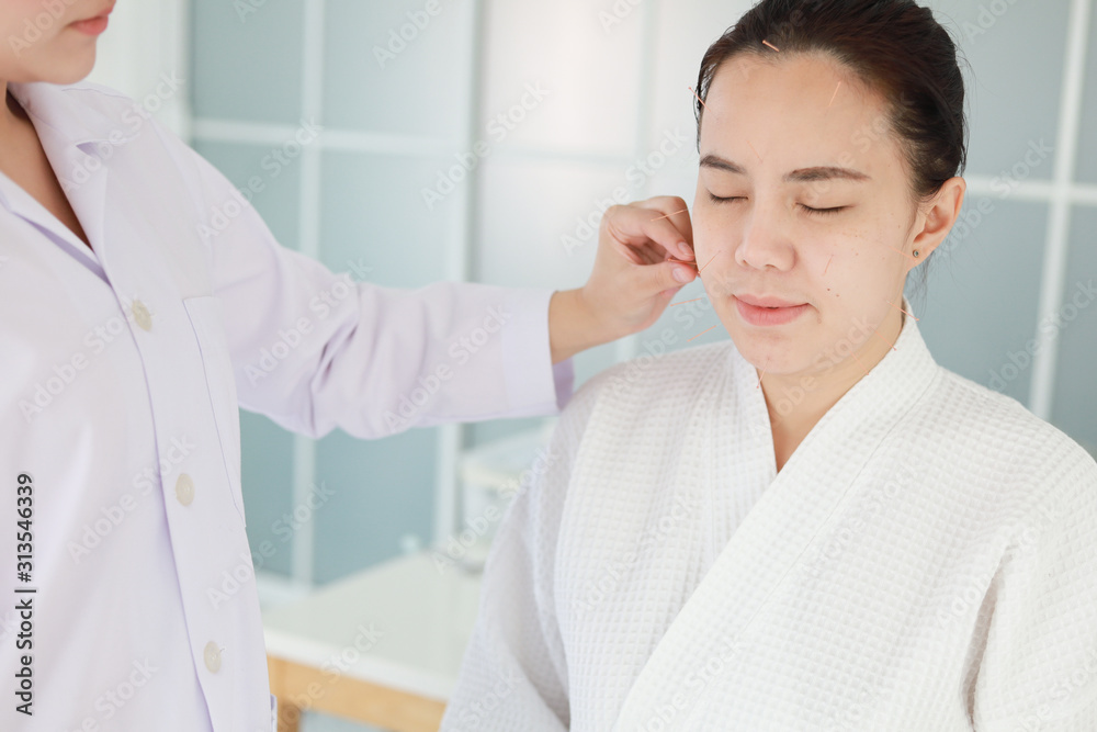 hand of doctor performing acupuncture therapy . Asian female undergoing acupuncture treatment with a line of fine needles inserted into the her face skin in clinic hospital