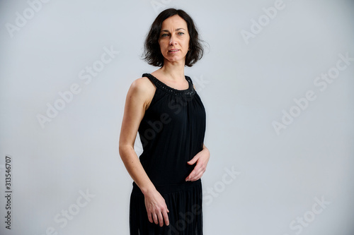 Portrait of a pretty brunette woman in a black dress on a white background. Shows emotions with hands in different poses right in front of the camera.