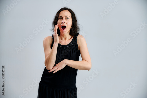 Portrait of a pretty brunette woman in a black dress on a white background. Shows emotions with hands in different poses right in front of the camera.