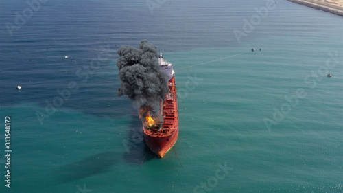 Aerial footage over Oil Tanker Ship Burning Under attack Aerial view with visual effect elements simulates realistic vision of Oil Tanker on fire with smoke in Gulf sea.