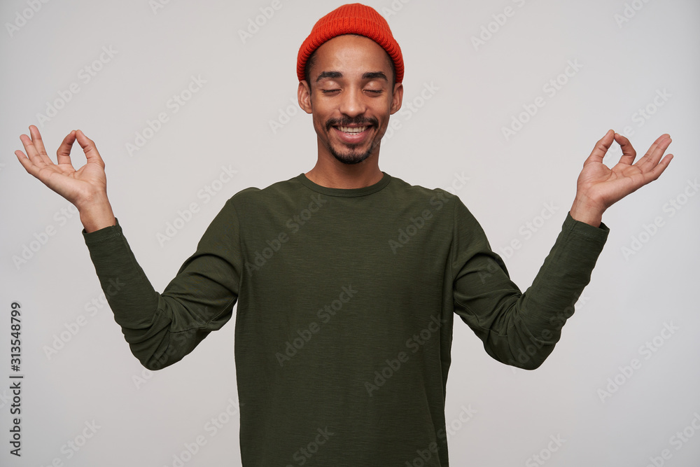 Portrait of young lovely bearded dark skinned brunette guy smiling positively and raising hands with mudra gesture while standing over white background, dressed in casual clothes Portrait of young lovely bearded dark skinned brunette guy smiling positively and raising hands with mudra gesture while standing over white background, dressed in casual clothes