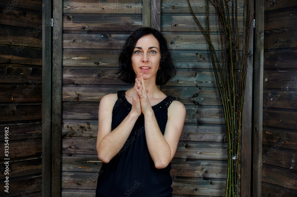 Portrait of a pretty smiling brunette woman in black dress on wooden background in vintage interior. Standing right in front of the camera with vivid emotions. Portrait of a pretty smiling brunette woman in black dress on wooden background in vintage interior. Standing right in front of the camera with vivid emotions.