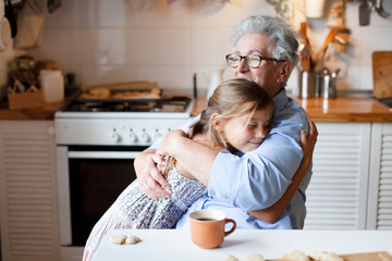 Grandmother hug child girl. Kid and senior woman baking in cozy home kitchen. Happy family enjoying kindness, tenderness, embracing. Lifestyle moment.
