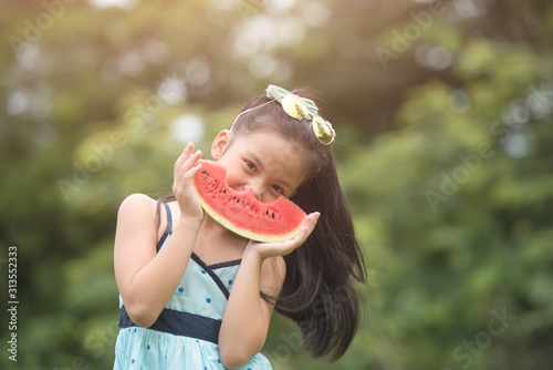 cute little girl eating watermelon on the garden in summertime. the kid smiles and starts to enjoy eating fruit in the field. healthy food concept..