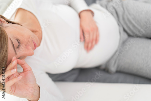 Pregnant tired exhausted woman with stomach and head issues at home on a couch, being sick.