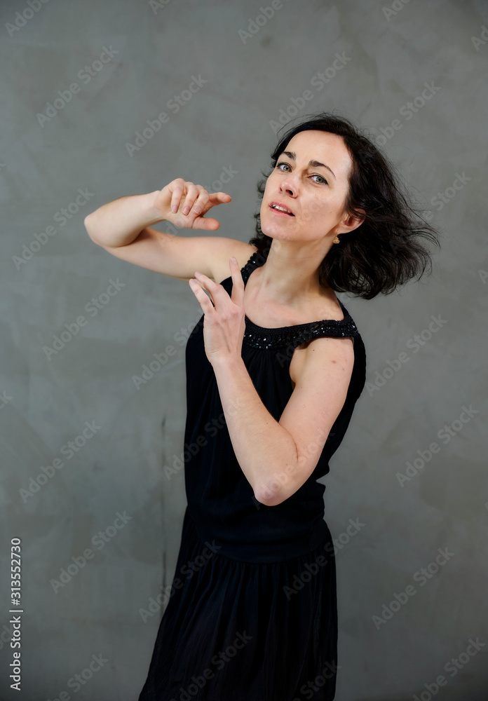 Model Standing right in front of the camera with vivid emotions. Vertical portrait of a cute smiling brunette woman in black dress on gray alternative background. Model Standing right in front of the camera with vivid emotions. Vertical portrait of a cute smiling brunette woman in black dress on gray alternative background.