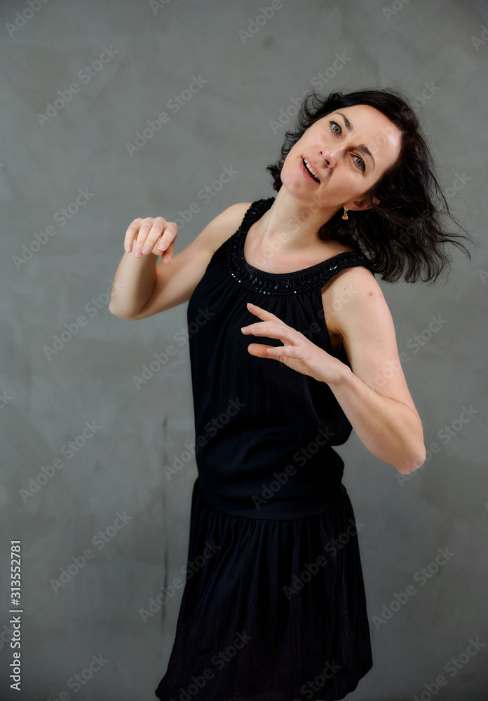 Model Standing right in front of the camera with vivid emotions. Vertical portrait of a cute smiling brunette woman in black dress on gray alternative background. Model Standing right in front of the camera with vivid emotions. Vertical portrait of a cute smiling brunette woman in black dress on gray alternative background.