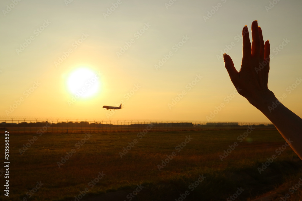Silhouette of woman's hand waving to the airplane against sunset sky