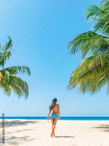 Beach vacation tourist enjoying Caribbean cruise travel destination walking in bikini on vertical blue sky background and palm trees  happy woman relaxing in Barbados.