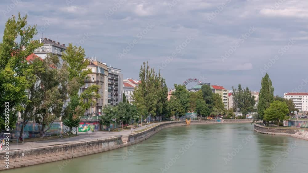 Vienna cityscape with the Danube channel timelapse in Vienna. Austria. Buildings with green trees and ferris wheel on a background Vienna cityscape with the Danube channel timelapse in Vienna. Austria. Buildings with green trees and ferris wheel on a background