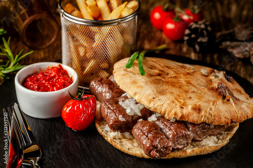 Turkish, oriental cuisine. Turkish tortilla, bun, pita bread with kebab and pickled onions. Serving in a restaurant on a black slate, on wooden table. background image, copy space photo