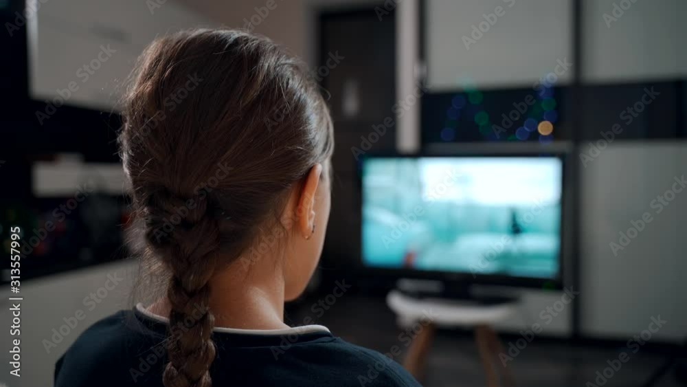 A young girl sitting on a sofa watching a movie on TV.