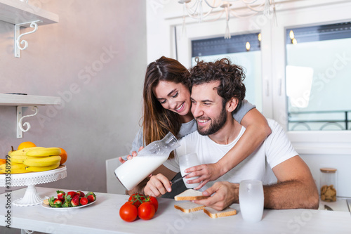 Romantic young couple cooking together in the kitchen having a great time together. Man and woman laughing and drinking milk in the morning with breakfast