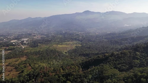 Flying over hill near mount gede pangrango in cisarua Bogor, passing rain forest and tea plantation with beautiful mountain in the morning. forward dolly motion photo