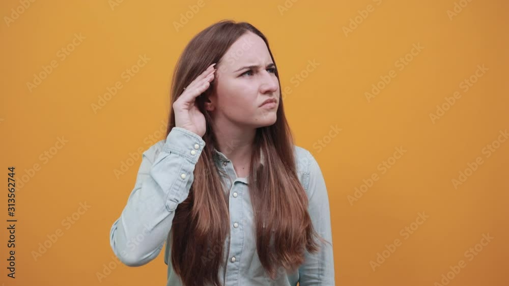 Pleasant caucasian lady wearing fashion shirt isolated on orange background in studio keeping palm near ear, listening. People emotions, lifestyle concept. Pleasant caucasian lady wearing fashion shirt isolated on orange background in studio keeping palm near ear, listening. People emotions, lifestyle concept.