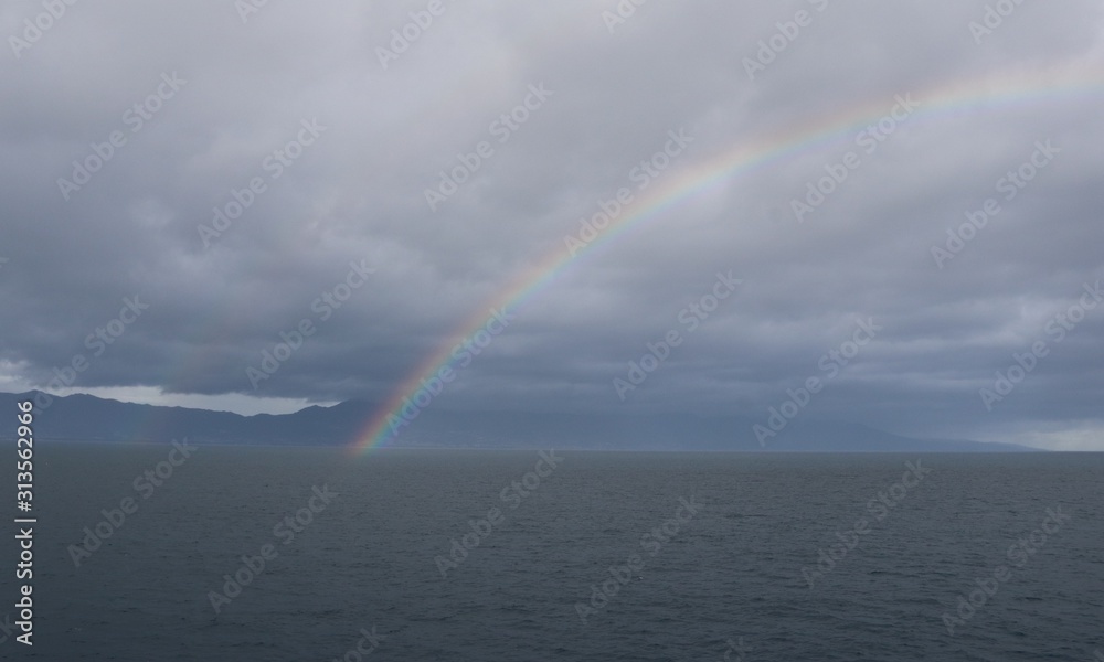 Rainbow arc against the background of a calm dark sea and rain low clouds