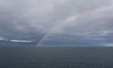 Rainbow arc against the background of a calm dark sea and rain low clouds