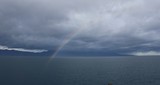 Rainbow arc against the background of a calm dark sea and rain low clouds