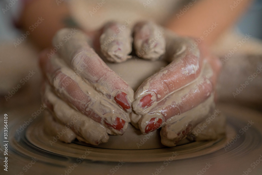 Close-up view of woman hands working on pottery wheel and making clay pot. Hands sculpts a cup from clay pot. Workshop on modeling on the potter's wheel.