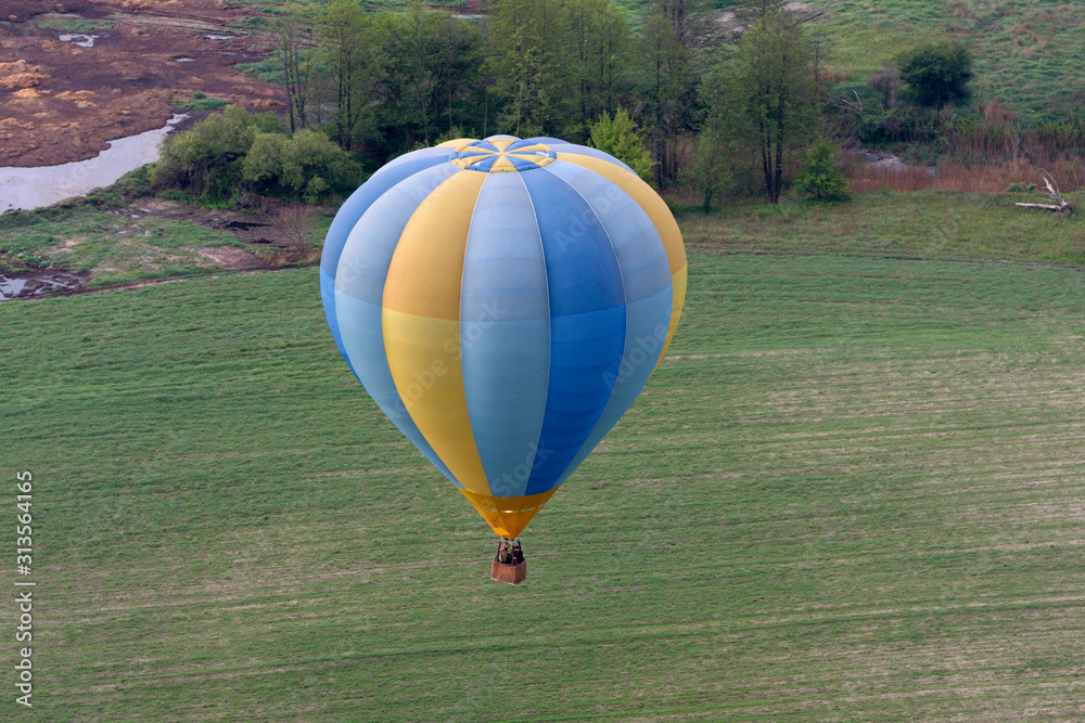 Obraz premium Hot-air balloon drifting toward the ground, field and trees on the background