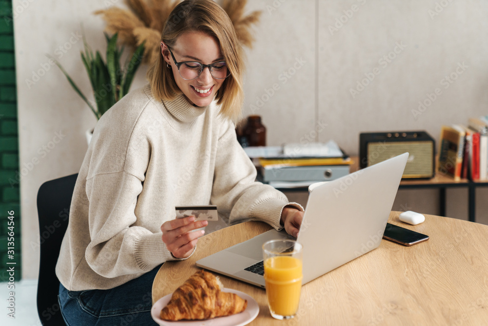 Photo of joyful blonde woman holding credit card and using laptop Photo of joyful blonde woman holding credit card and using laptop
