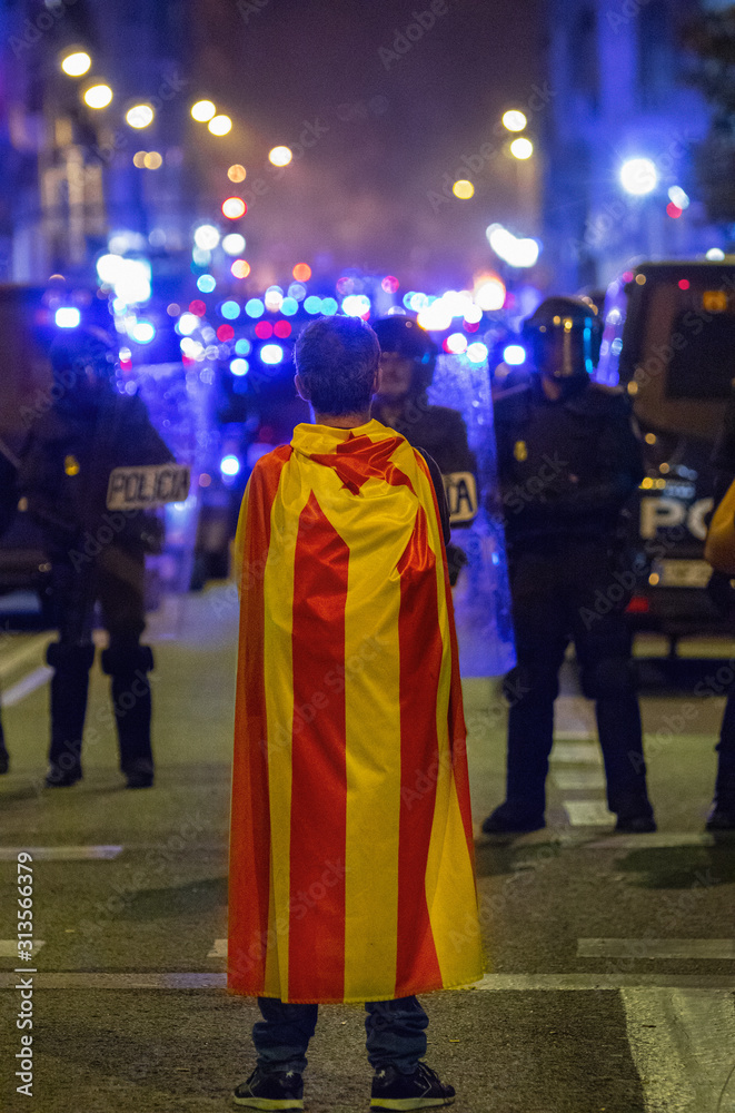 18th October - A Catalan man stands defiant against police wall. Fires can be seen in background 18th October - A Catalan man stands defiant against police wall. Fires can be seen in background