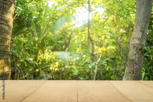 Fototapeta Naklejka Na Ścianę i Meble -  Pine wood table top (Bar) with blur on green palm leaves or tree in tropical forest with bokeh light at background