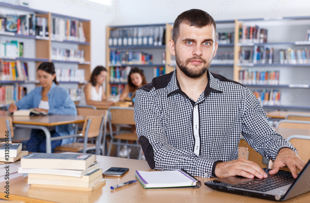 Fototapeta premium Young male student working with laptop and books in university library