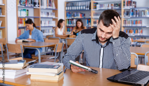 Portrait of upset tired male student preparing for exam in university library