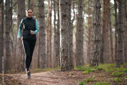 Beautiful Smiling Woman Running on the Forest Trail at Cold Autumn Evening. Sport and Active Lifestyle.