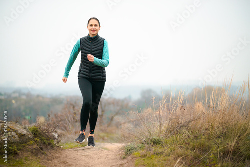 Beautiful Smiling Woman Running on the Mountain Trail at Cold Autumn Evening. Sport and Active Lifestyle.