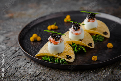 Murais de parede Luxurious appetizer of quail eggs with a paste of squid, shrimp and black caviar on potato and cheese chips