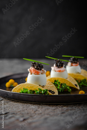 Fotografia Luxurious appetizer of quail eggs with a paste of squid, shrimp and black caviar on potato and cheese chips