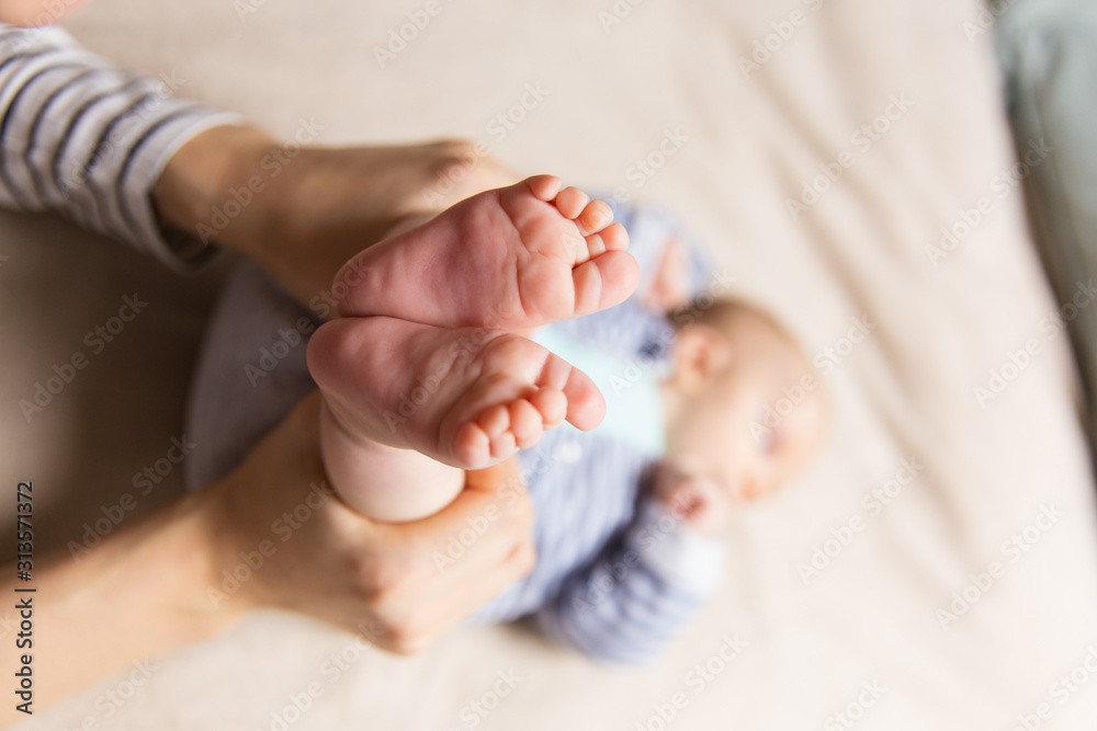 Closeup of baby feet and human hands holding kid legs. Cute little child in home interior. Healthy skin or baby care concept - obrazy, fototapety, plakaty 