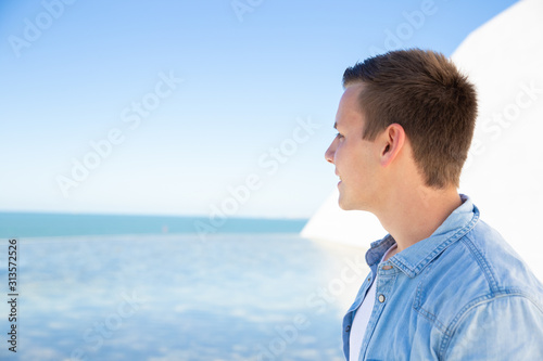 Pensive student guy relaxing at sea, looking at horizon. Handsome young man in casual walking along promenade. Male portrait or advertising concept