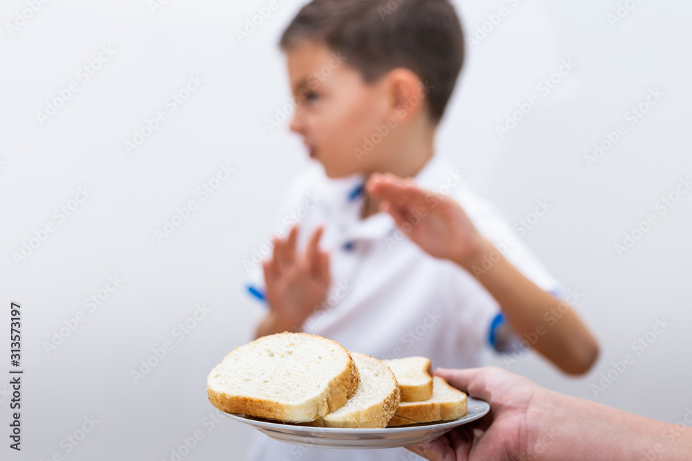 Gluten intolerance and diet concept. Kid refuses to eat white bread. Selective focus on bread. Kid on gluten free diet is saying no thanks to toast. Gluten intolerance and diet concept. Kid refuses to eat white bread. Selective focus on bread. Kid on gluten free diet is saying no thanks to toast.