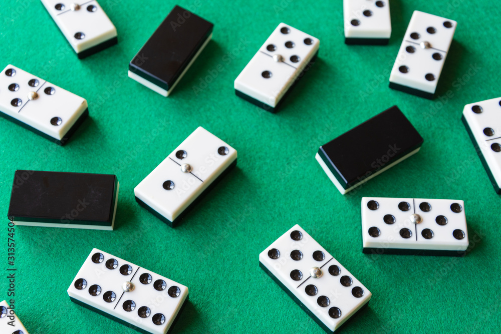 Top view of domino pieces, covered and uncovered, unfocused those in the background, on green mat to play horizontally Top view of domino pieces, covered and uncovered, unfocused those in the background, on green mat to play horizontally