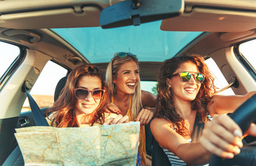 Three female friends enjoying traveling at vacation in the car.