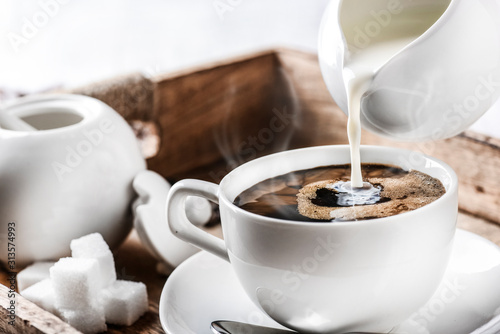 Coffee cup and roasted coffee beans on wooden tray. Pouring milk.