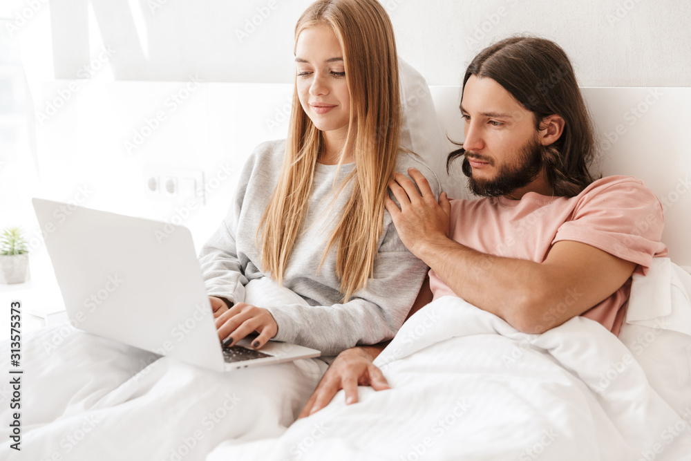 Loving couple in bed using laptop computer indoors at home. Loving couple in bed using laptop computer indoors at home.