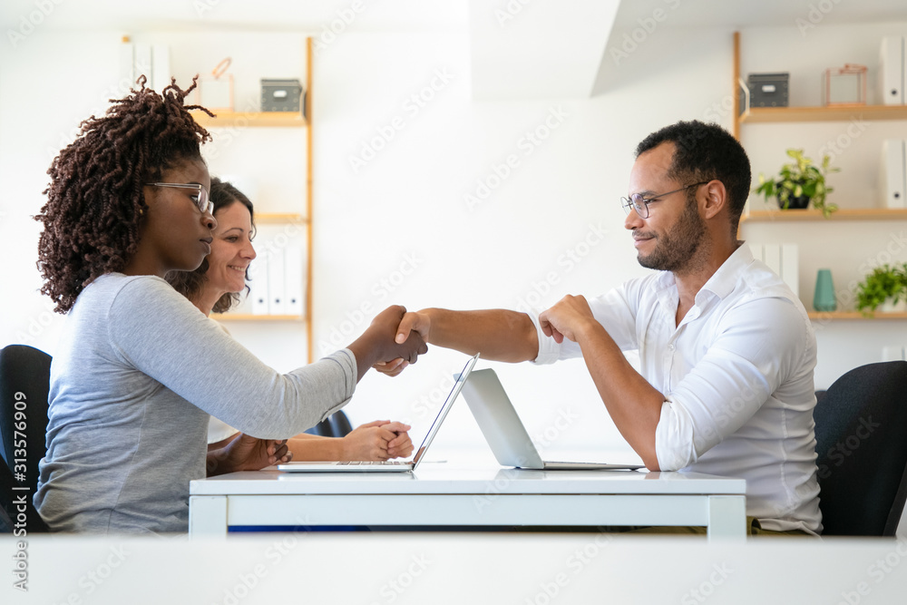 Cheerful business partners shaking hands. Confident young people reaching agreement. Agreement concept Cheerful business partners shaking hands. Confident young people reaching agreement. Agreement concept