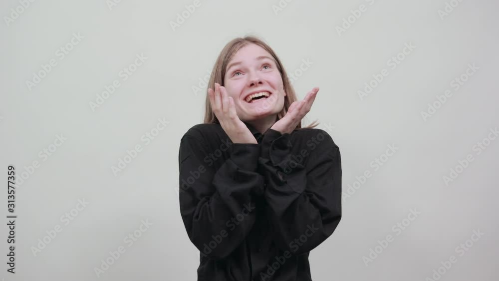 Cheerful charming lady in black shirt keeping palms over chin, smiling, looking at camera isolated on gray background in studio. People sincere emotions, lifestyle concept. Cheerful charming lady in black shirt keeping palms over chin, smiling, looking at camera isolated on gray background in studio. People sincere emotions, lifestyle concept.