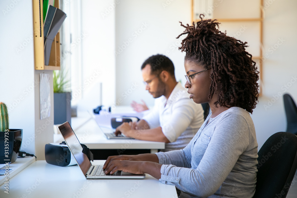 Focused young woman typing on laptop. Side view of concentrated worker using laptop at office. Technology concept Focused young woman typing on laptop. Side view of concentrated worker using laptop at office. Technology concept
