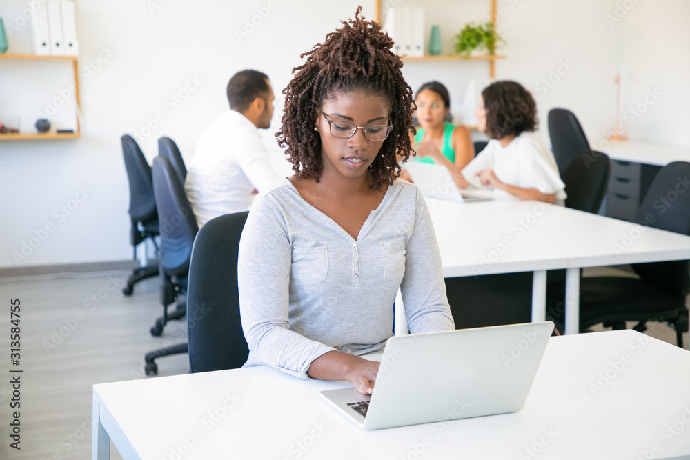 Front view of focused attractive worker typing on laptop. Thoughtful young woman with dreadlocks working with laptop at office. Technology concept Front view of focused attractive worker typing on laptop. Thoughtful young woman with dreadlocks working with laptop at office. Technology concept